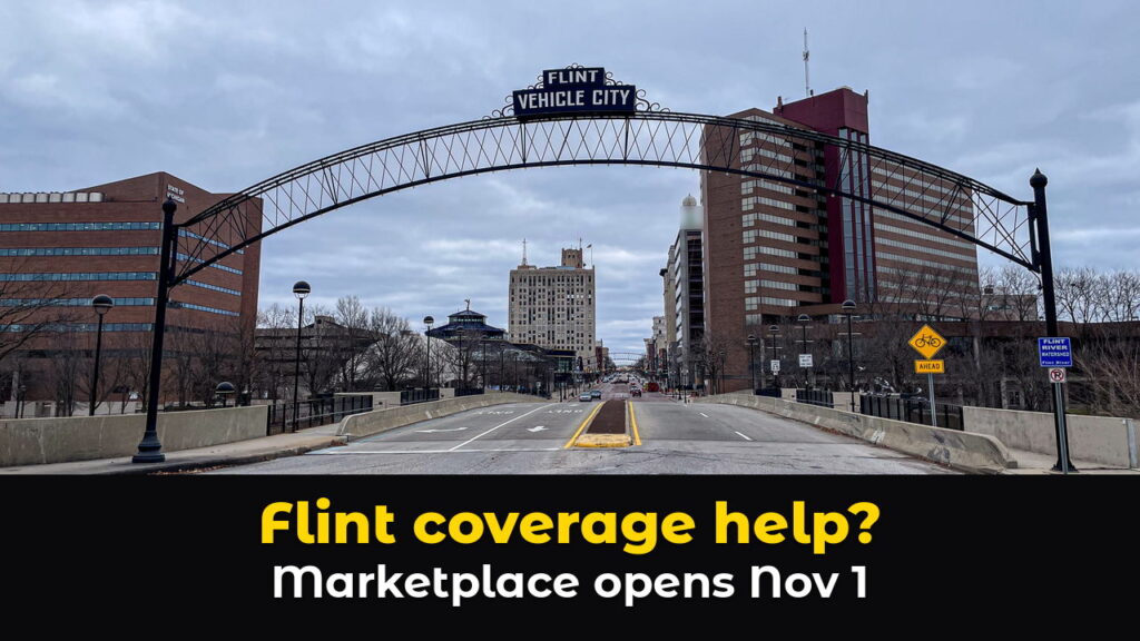 The steel Flint Vehicle City arch spans Saginaw Street in downtown Flint, Michigan, with brick office towers on both sides under a cloudy sky, above hook text: Flint coverage help? Marketplace opens Nov 1.