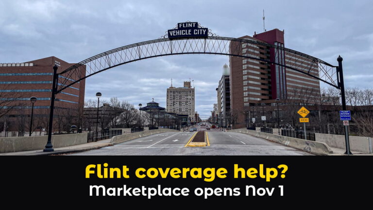 The steel Flint Vehicle City arch spans Saginaw Street in downtown Flint, Michigan, with brick office towers on both sides under a cloudy sky, above hook text: Flint coverage help? Marketplace opens Nov 1.